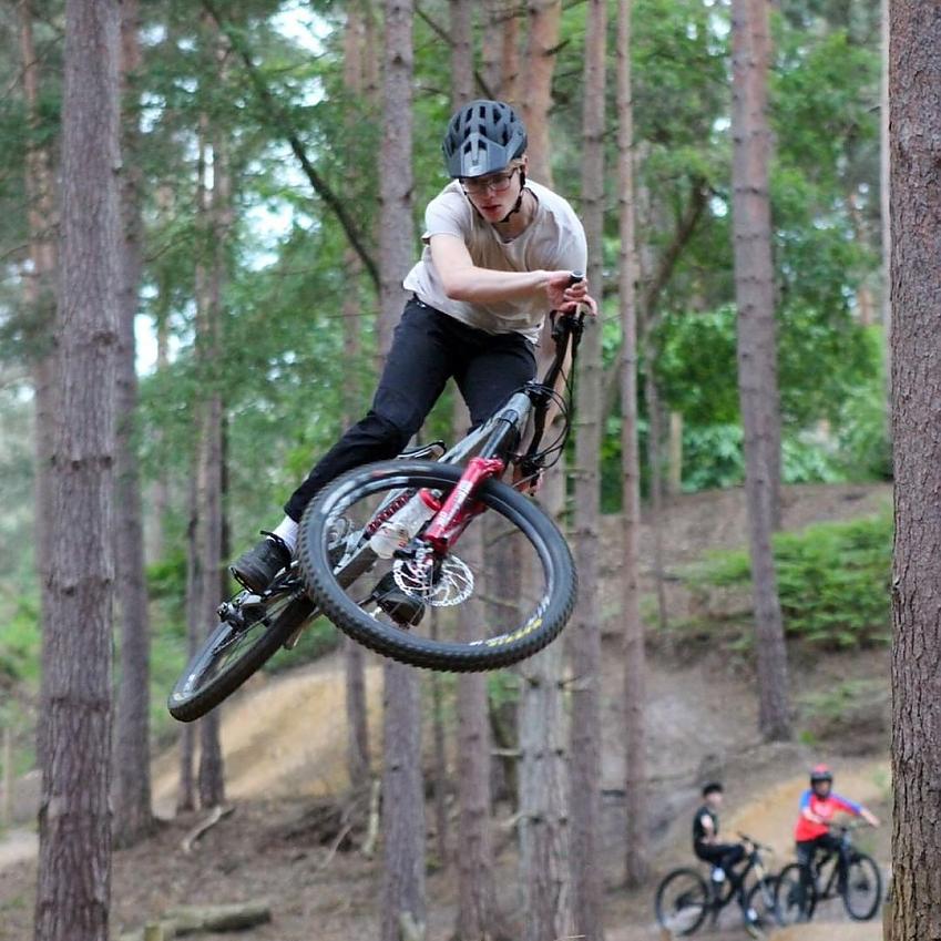 A young man is flying through the air on his mountain bike in a forest setting
