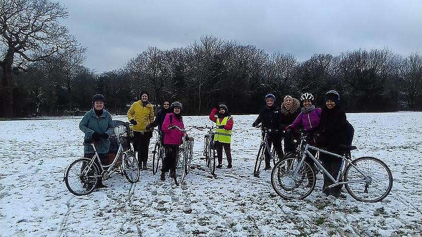 A group of women are posing with their bikes in a snowy field. They are all smiling despite the cold wintry weather