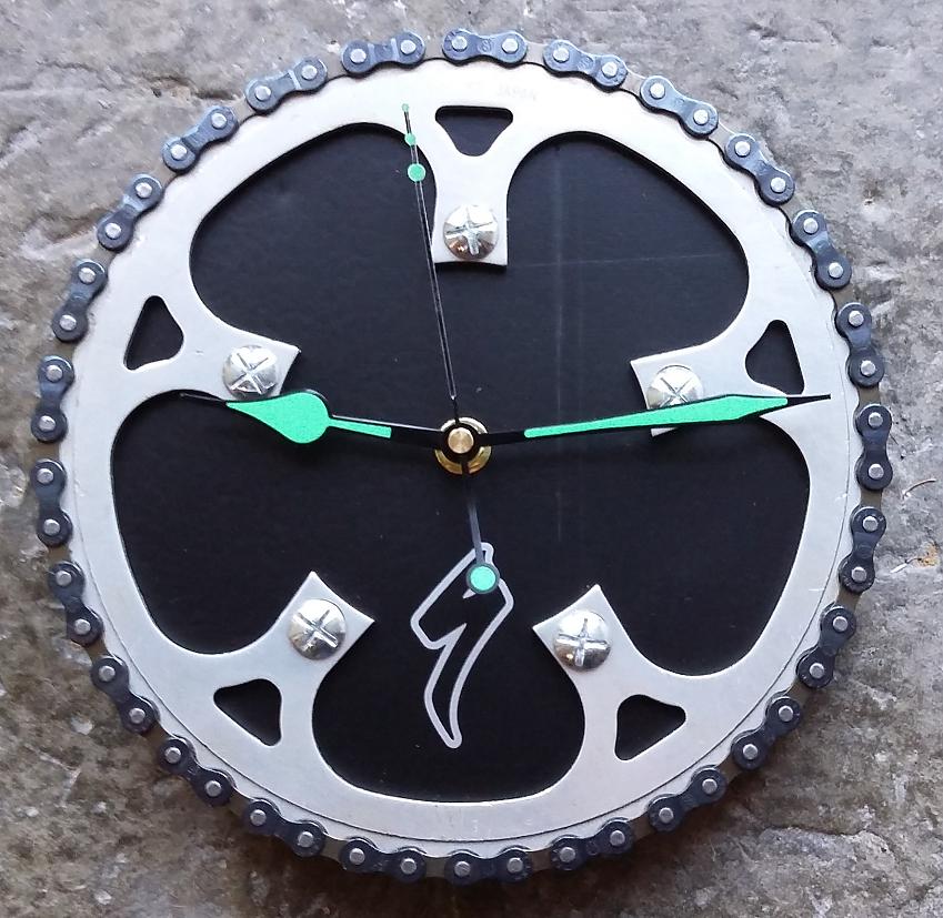 A clock made from bicycle parts with green hands 