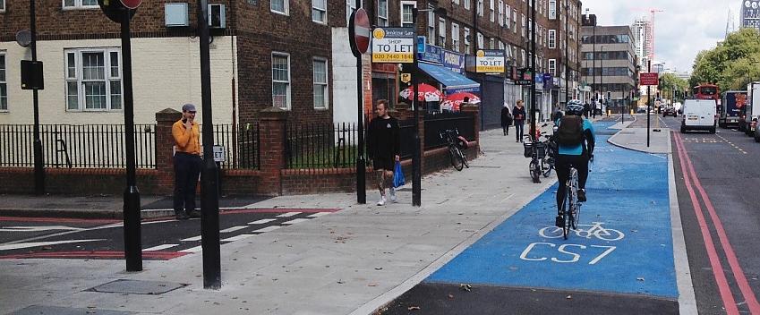 A side road turning into a busy London street is so designed that traffic has to give priority to pedestrians and cyclists, with the stop and give way signs prior to the pavement and cycle track