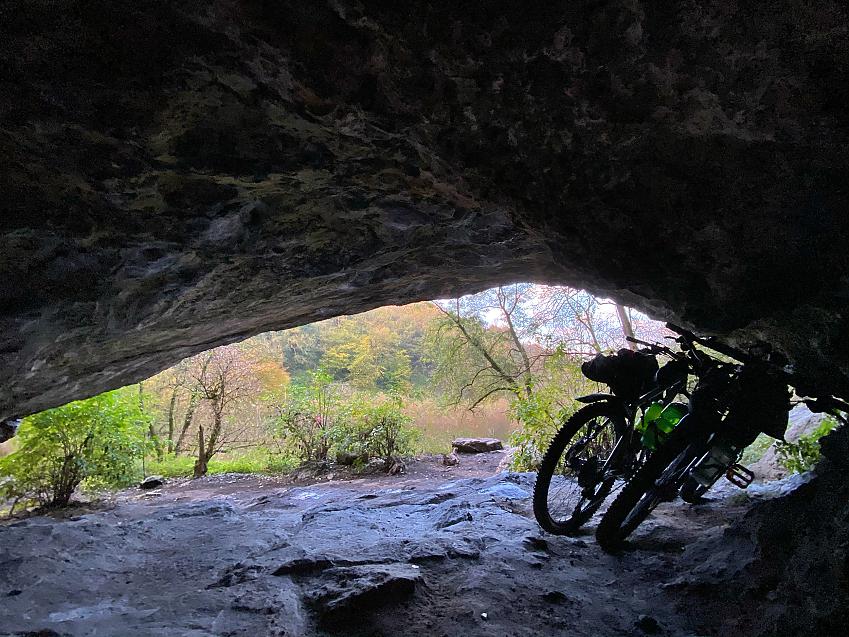 Two bikes in the mouth of a cave, taken from inside the cave looking out at the wooded scenery