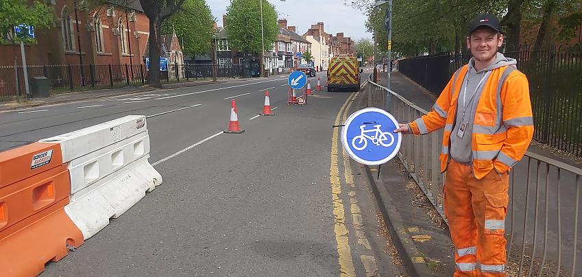 Highway worker holds cycling sign next to temporary cycle lane