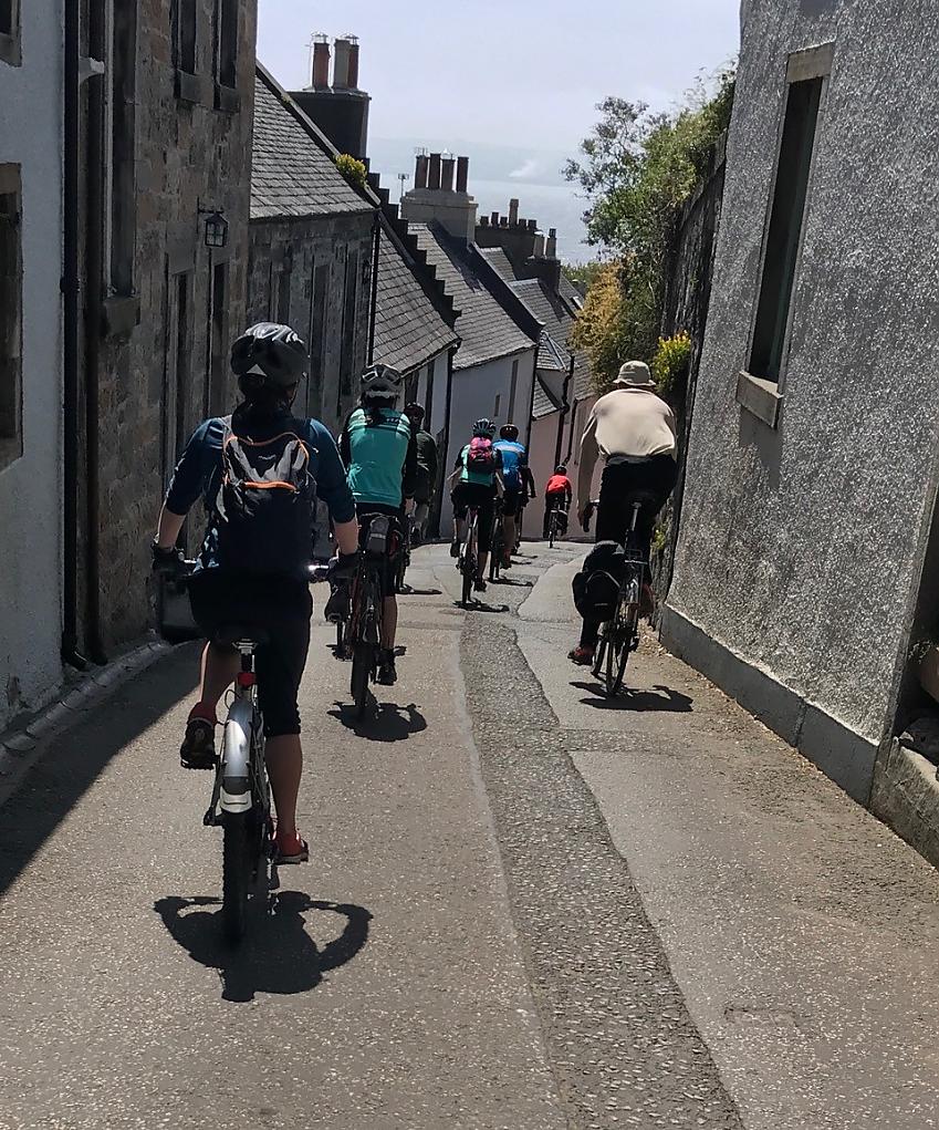 A group of cyclists is cycling along a very narrow road in Fife