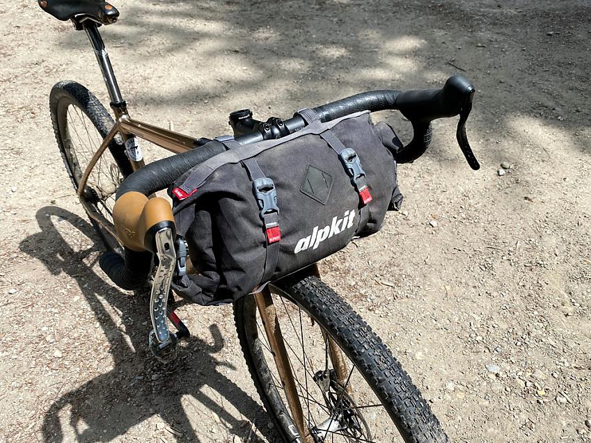 A bicycle boasts a big black nylon back with two clips either side, the word 'Alpkit' is embossed on it in white