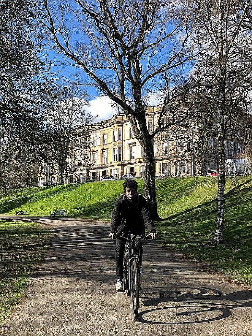 A man cycles towards us along a path in an urban park
