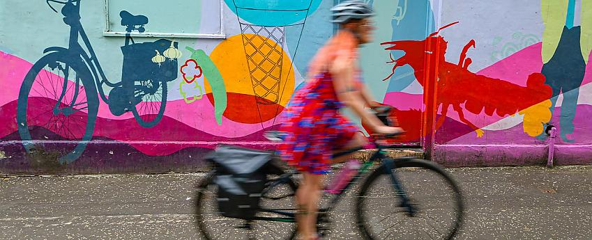 A woman cycles past a bright wall mural