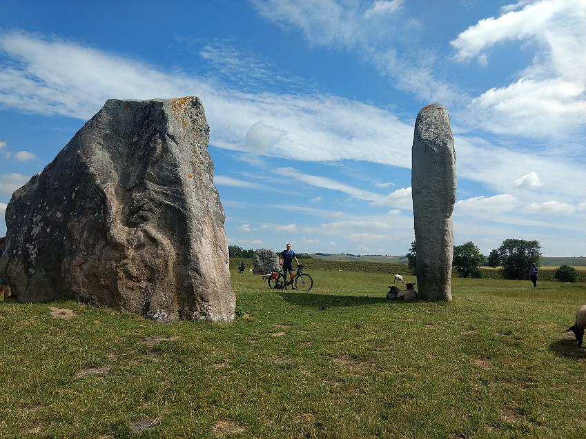 A man poses with his bicycle among Neolithic monuments while sheep graze around him