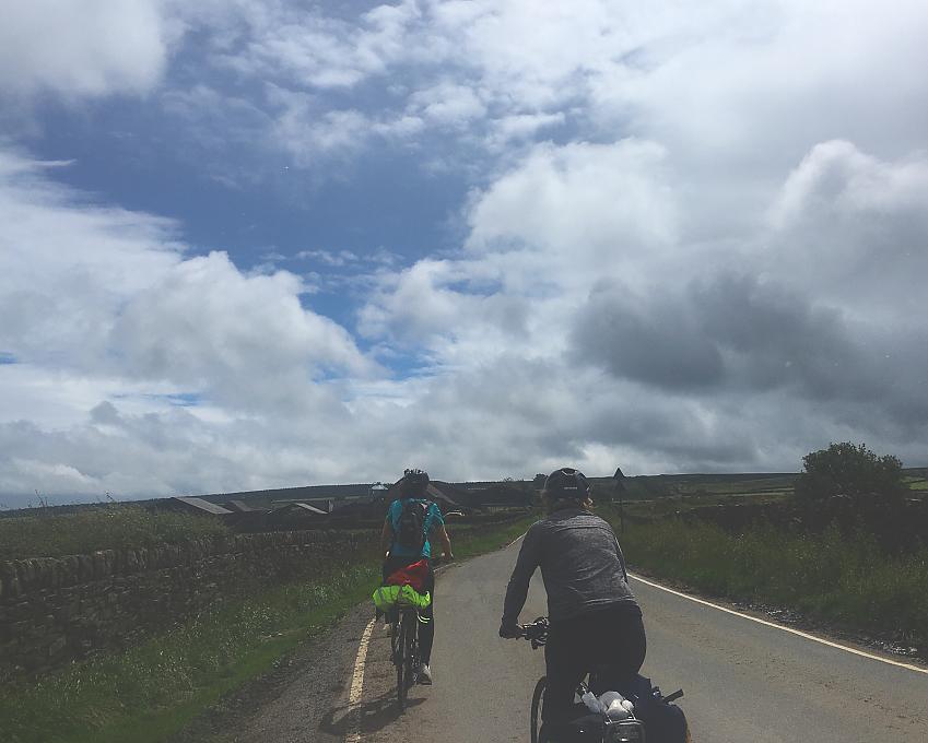 Two women are cycling along a narrow road in the Peak District