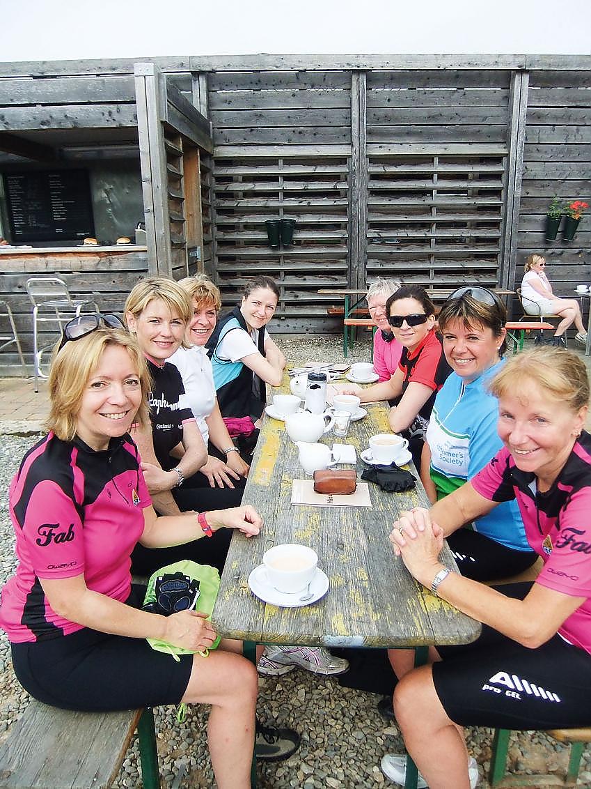 A group of women in cycle clothing sitting around a cafe table drinking tea and coffee