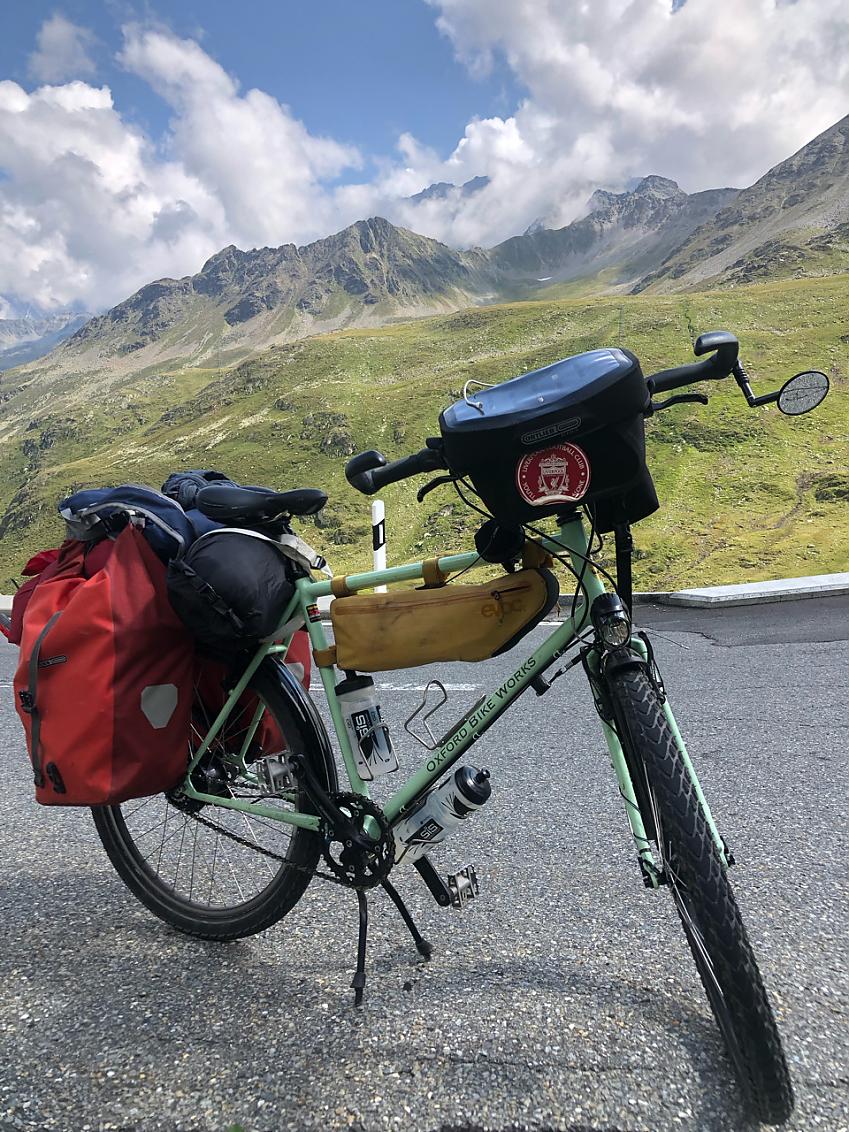 Candy Whittome’s custom-made expedition bike parked with an Alpine landscape and blue skies behind