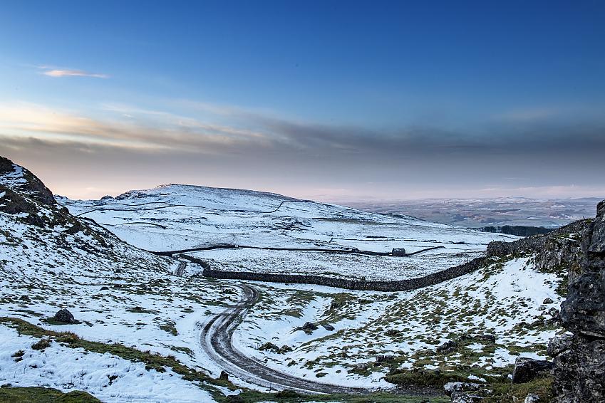 A panoramic shot of the Yorkshire Dales in winter. It's dusk and the sun is setting; there's snow lying on the ground