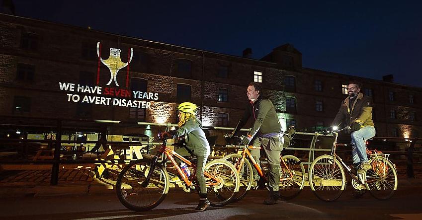 People cycle past a projection on Holyrood building saying "We have seven years to avert disaster"