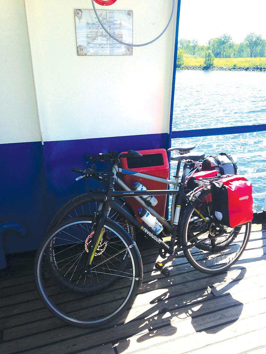 Two bikes are leaning on the deck of a ferry. They both have packed panniers ready for touring