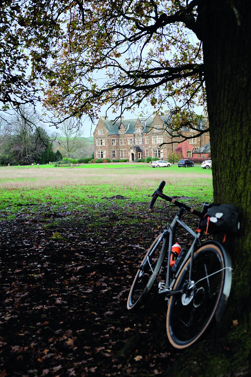 A bike rests against a tree in parkland facing a stately home