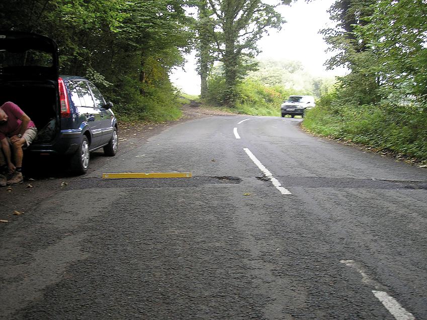 A metre-long spirit level lays across the left-hand lane of a country road. there are potholes to the right of it