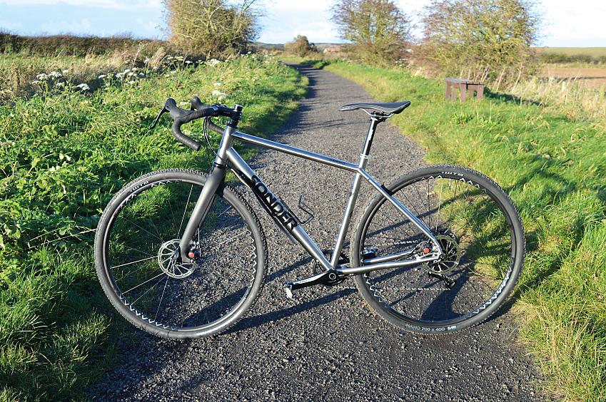 Sonder Camino Ti gravel bike in silver, propped up on a gravel path