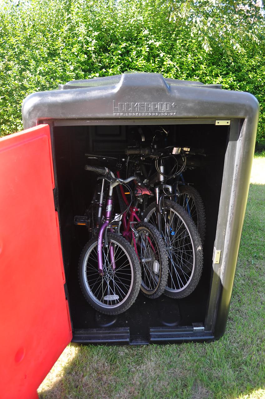 A lockerpod in a garden, the door is open and there are four bikes in it, two adult and two kids