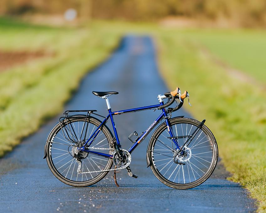 A blue touring bike with drop handlebar and rear rack propped up on a wet road