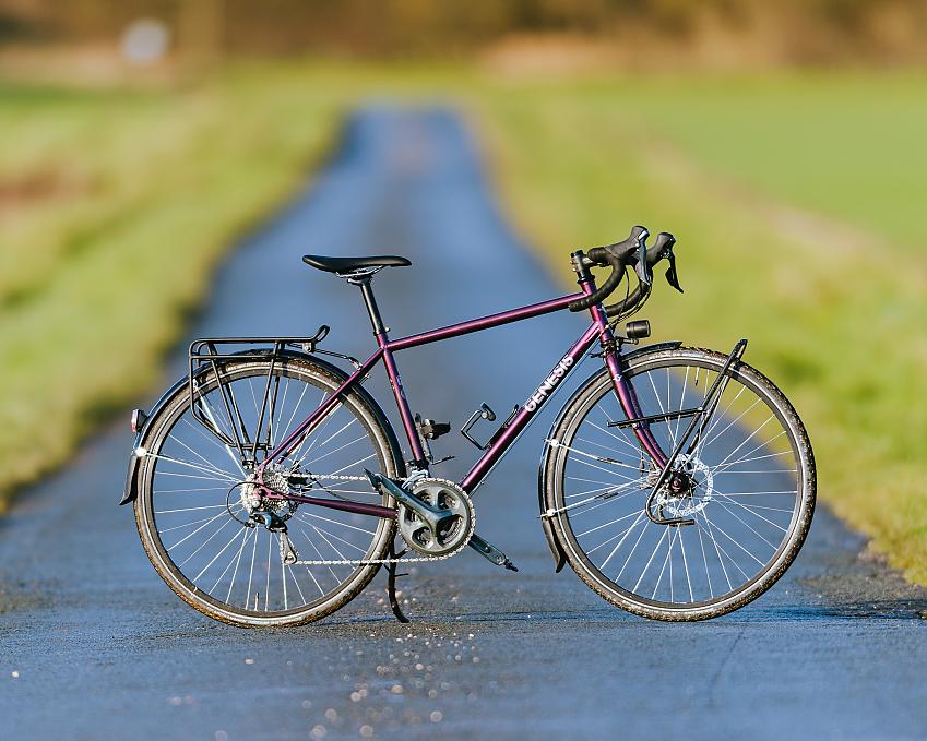 A purple touring bike with drop handlebar and rear rack is propped up on a wet road