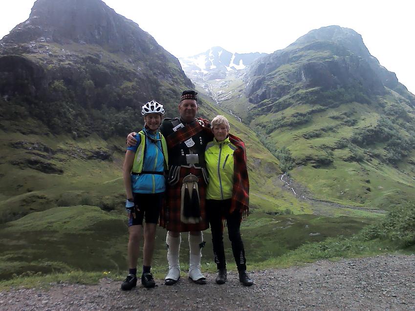 Two women in cycling kit pose with a man in a kilt at Glen Coe