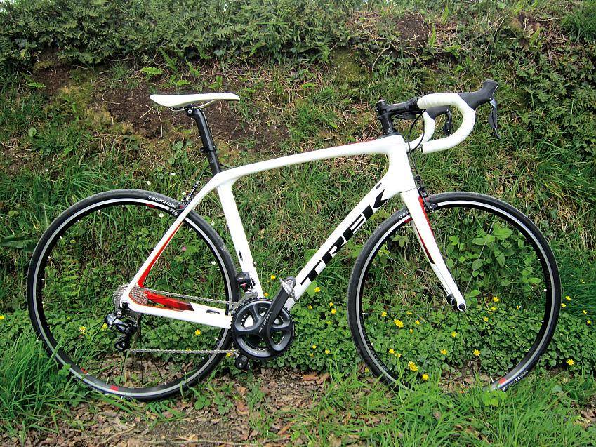  Trek Domane SLR7, a white road bike with some red highlights, leaning against a grass verge