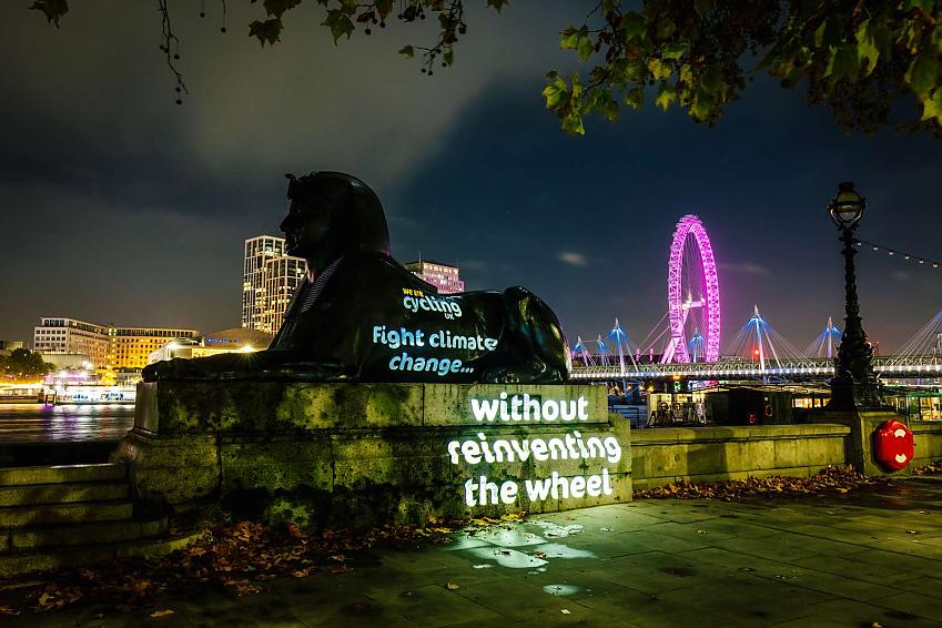 The sphinx statue on the Embankment in London at night. Projected onto the statue are the Cycling UK logo and the word 'Fight climate change without reinventing the wheel'. In the background are the Hungerford Bridge and London Eye all lit up