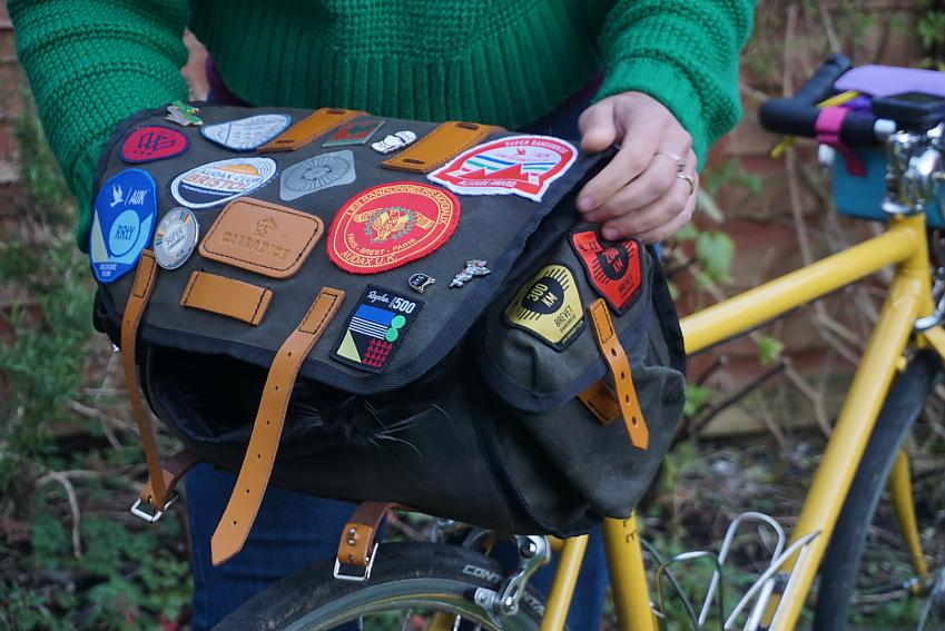 A close-up of a large black saddle bag covered with badges and attached to a yellow bike