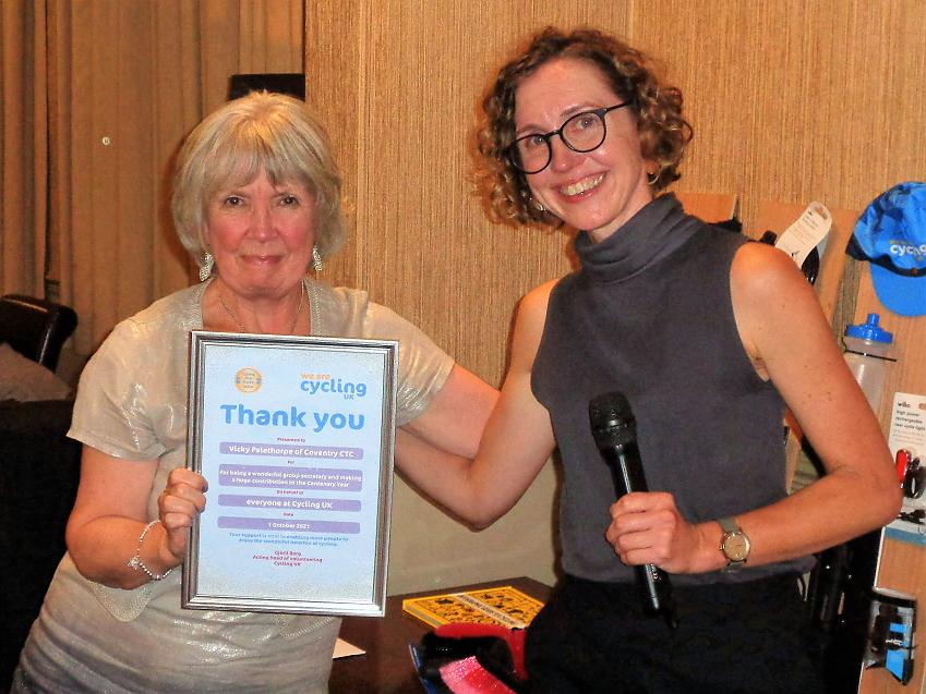 Two women are posing with a Certificate of Thanks in a frame, which the woman on the right has presented to the one on the left