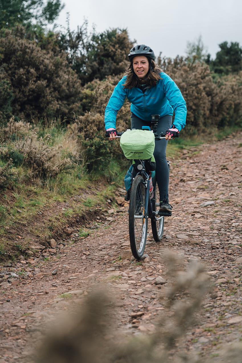 A woman cycling on a stony, rough path.