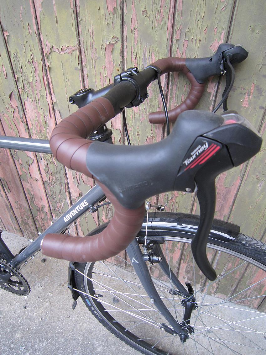 A close-up of the Adventure Flat White's handle bar from the side, showing the brown bar tape, gear shifters and brake levers