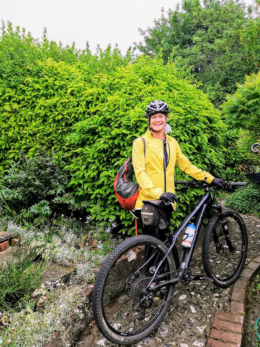 A woman holding a mountain bike, standing in front of a garden; she is smiling