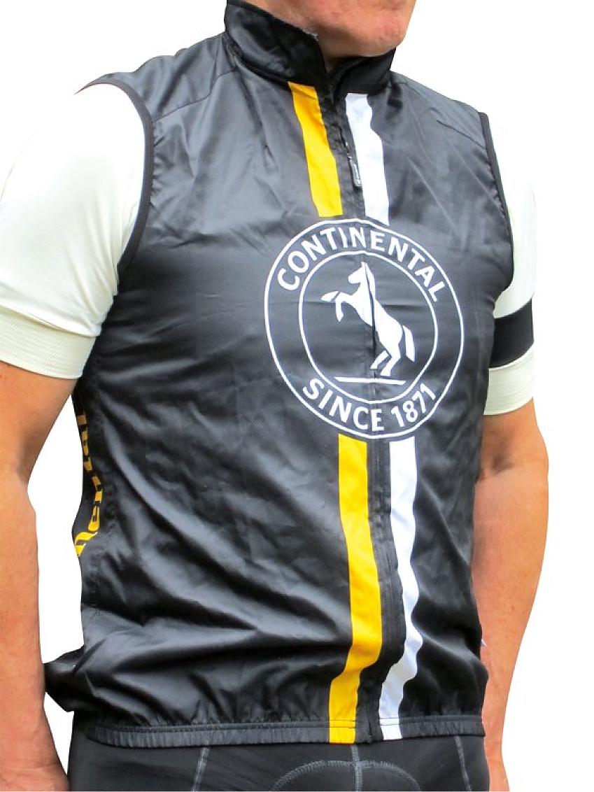 A man wears a black gilet with vertical yellow and white stripes and a dancing horse logo 