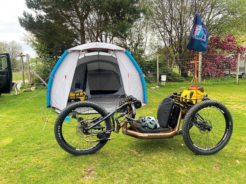 A hand cycle rests in front of a large tent on a campsite
