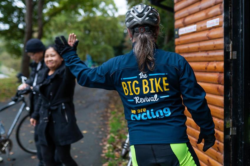 The back of a lady wearing a Cycling UK jacket and another lady in the background with a helmet on