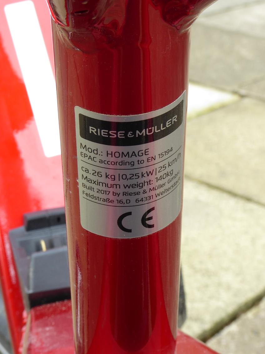 A close-up of a red downtube on an e-bike showing the legally required conformity plate displaying manufacturer and power output