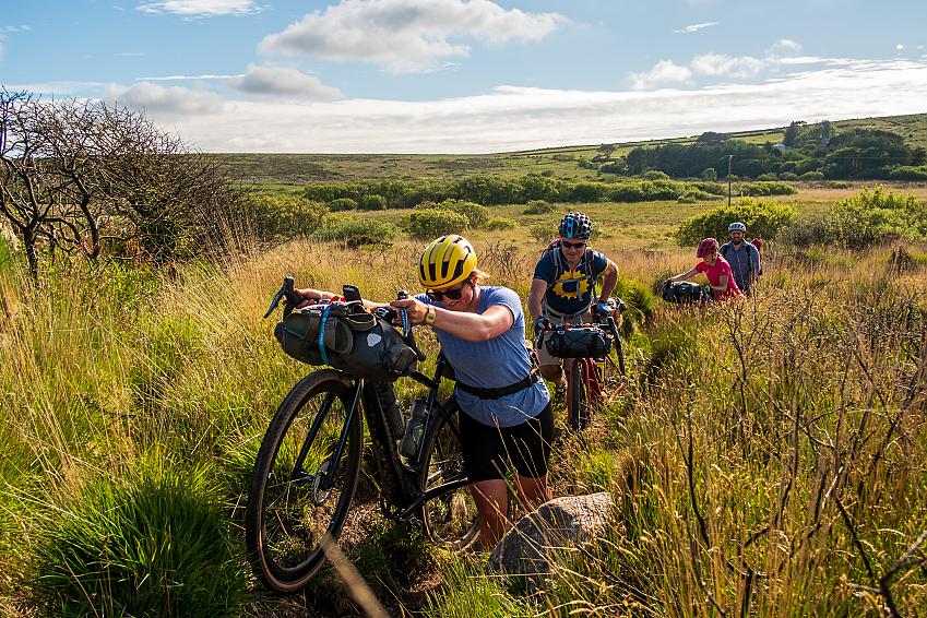 A group of cyclists push their bikes through thick undergrowth