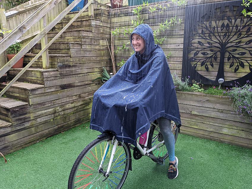 A woman sits on a bike in a garden wearing a rain poncho