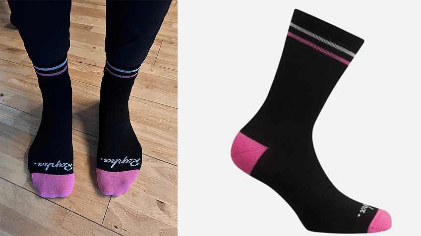 Two black socks with pink features and word Rapha written above the toes on two feet with a wooden floor background