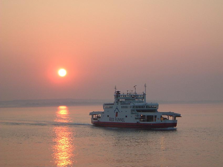 A Red Funnel ferry on the sea at sunset, with the sun shining off the sea