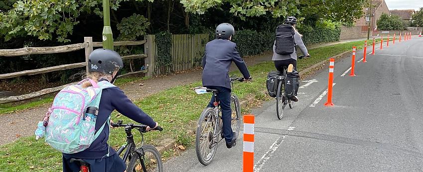 Three cyclists in a cycle lane protected by thin bollards known as wands