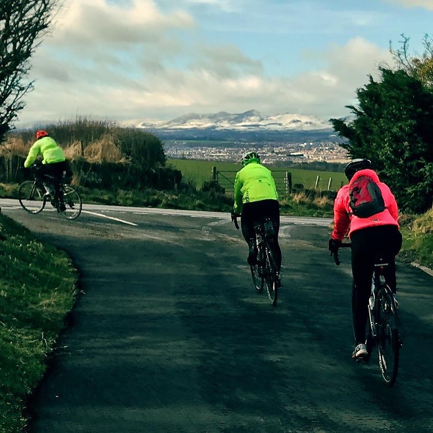 Three cyclists are cycling along a road approaching a junction. They are all wearing winter cycling jackets.