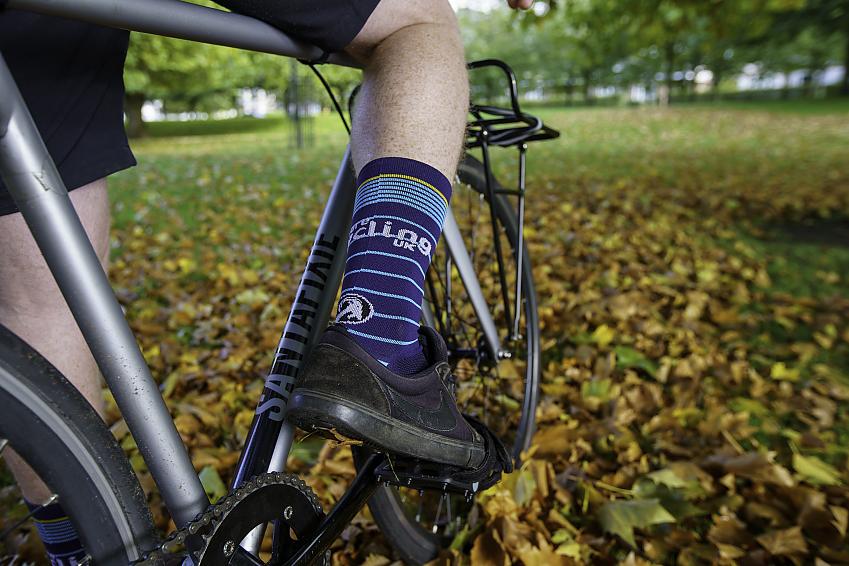 Cycling UK Stolen Goat sock in a shoe resting on the pedl of a bike above a bed of fallen russet leaves