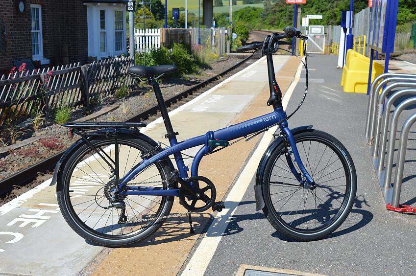 The Tern blue folding bike propped up on its kickstand on railway platform
