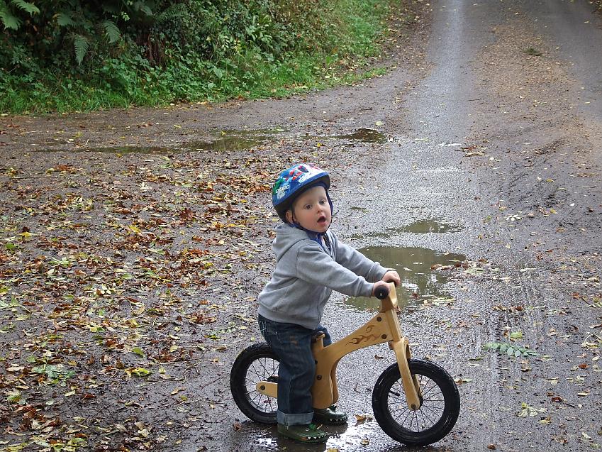 A toddler in a blue helmet on a balance bike with his feet touching the ground