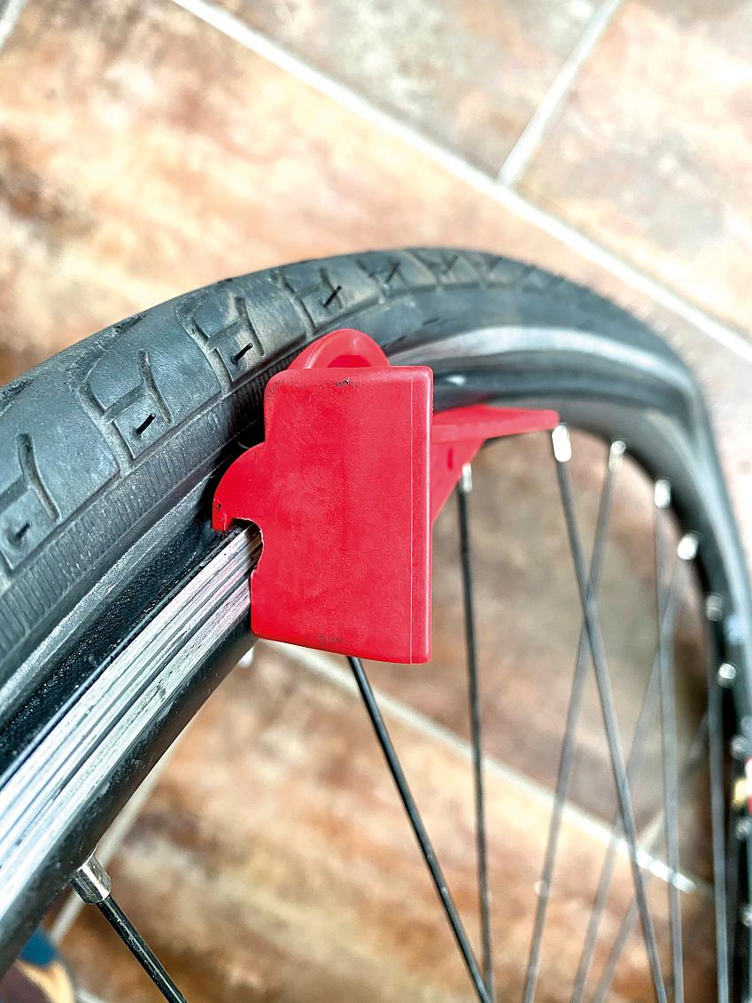 The Tyre Glider tool, which is bright red, is shown in use, pushing the tyre away from the wheel rim so it can be removed