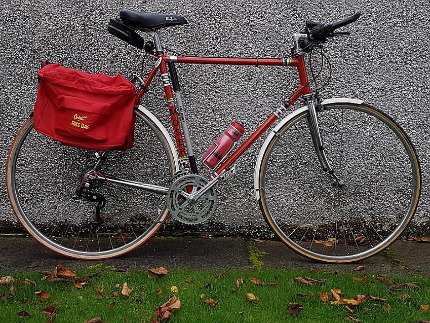 A red Italian Moser cycle, with a red pannier and red water bottle; the bike is leaning against a wall