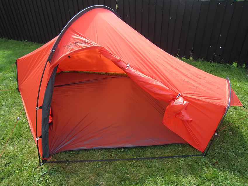 A bright orange 1-person tent is pitched on grass, the door is unzipped