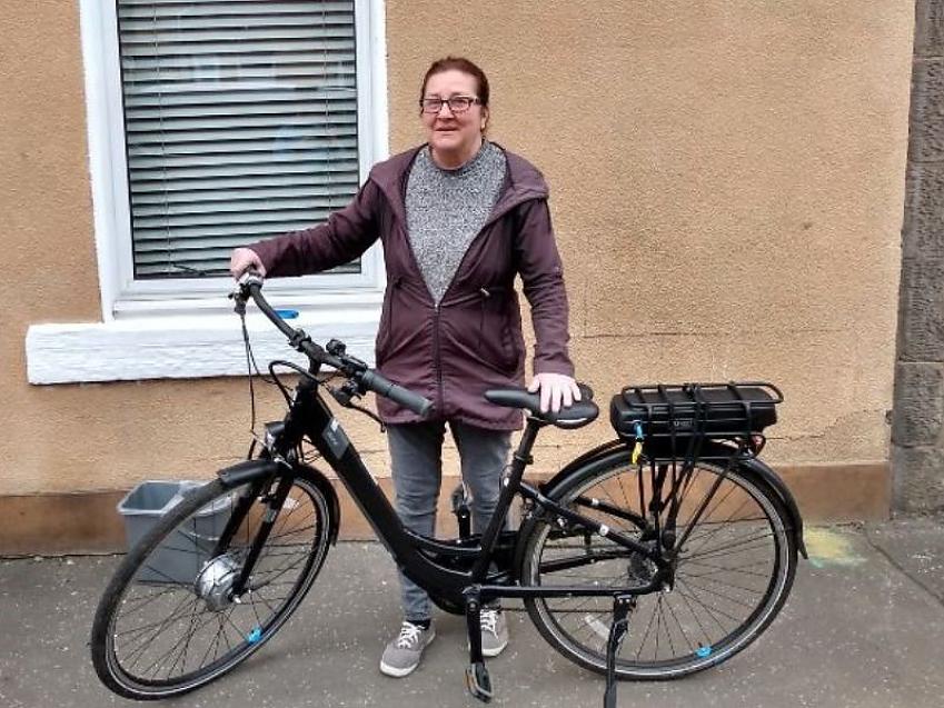 A woman holding an e-cycle; she is outside a house