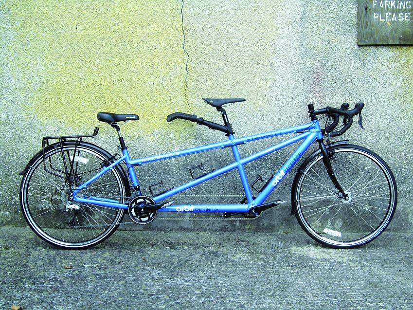 Orbit Velocity Comp, a blue tandem bike leaning against a concrete wall with a crack in it