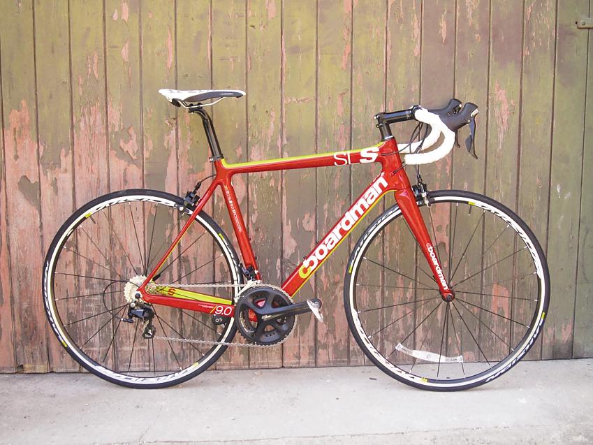A bright orangey-red and yellow road bike is leaning against a wooden fence